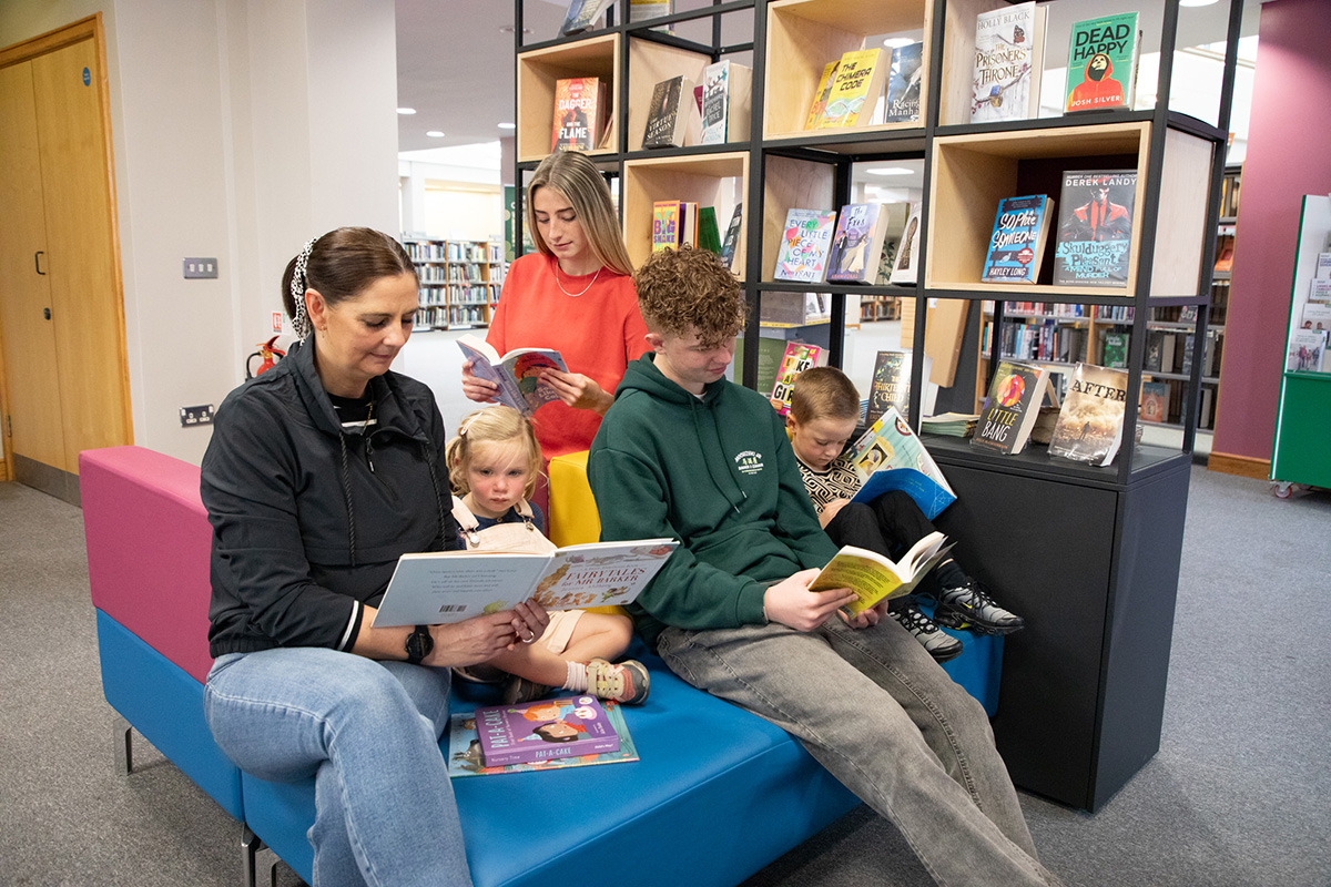 A mother and children all reading books in a library